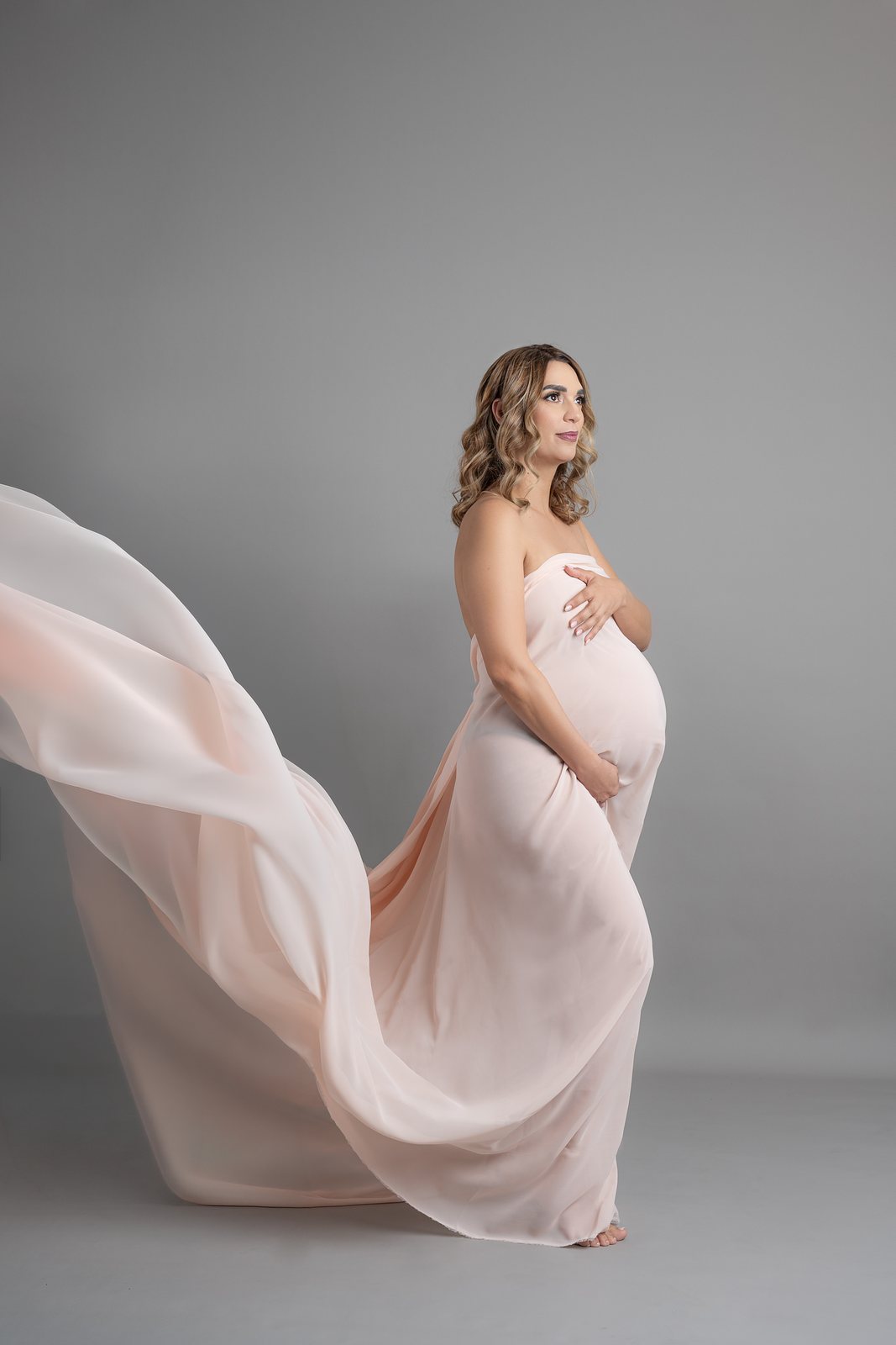 Sesión de maternidad en estudio con tela rosa en movimiento